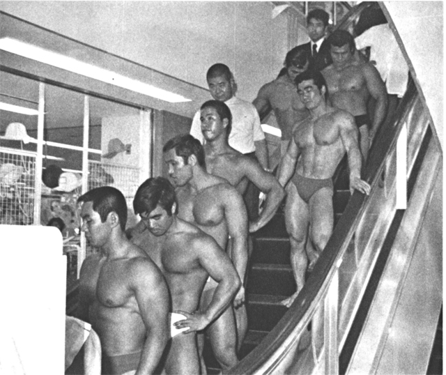 屋上から２階の特設ステージまで裸のままエスカレーターで降りる選手たち。各売場の女店員たちが興味深そうにながめていた。